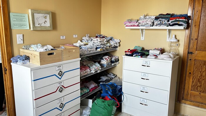 Des étagères débordent de petits vêtements de bébés. 