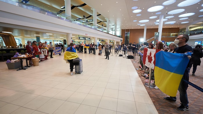 People hold Canadian and Ukrainian flags in the airport terminal.