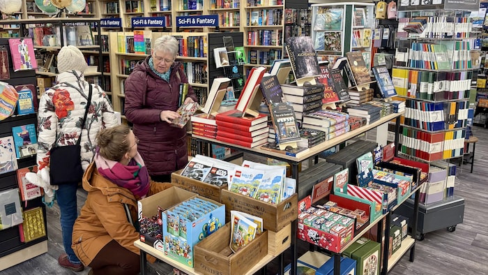 Trois personnes dans une librairie au milieu des livres.