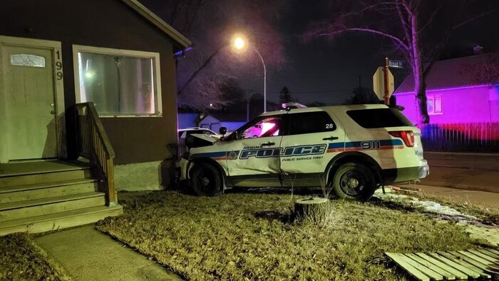 Une voiture de police endommagé devant les murs d'une maison.