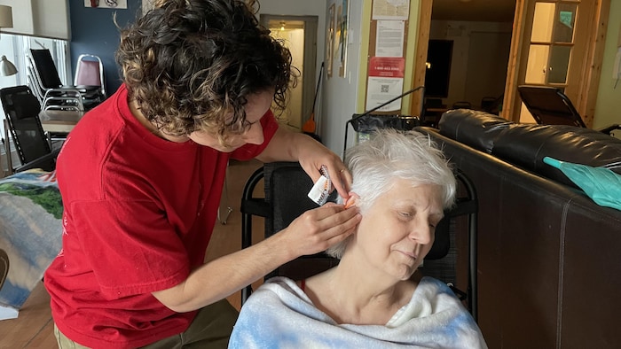 L'acupuncteur Félix Dénommé fait un traitement selon l'approche NADA à une participante. Elle est assise sur une chaise et a des aiguilles dans l'oreille. 