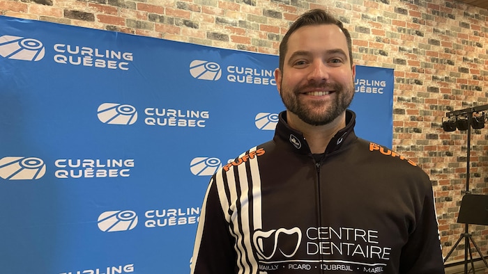 Adam Rocheleau debout dans une salle souriant pour se faire prendre en photo.