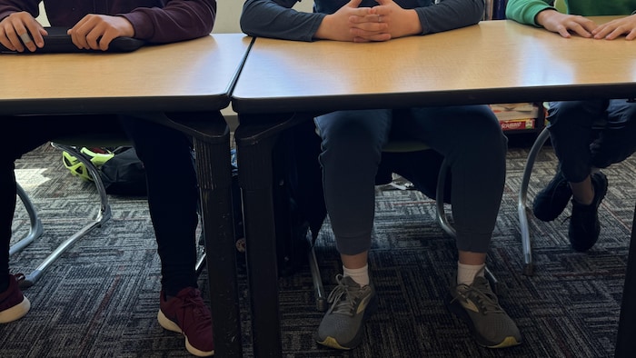 Les pieds de certains jeunes garçons sous la table de classe.