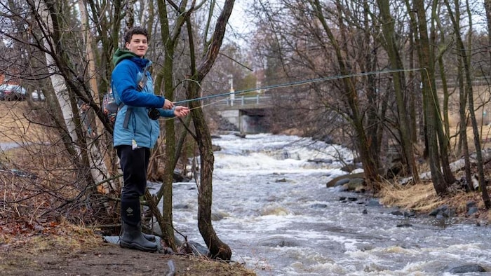 Un jeune homme pêche la truite dans un ruisseau.