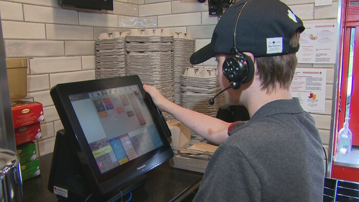 Un jeune regarde un écran d'ordinateur qui sert à prendre les commandes dans un restaurant.