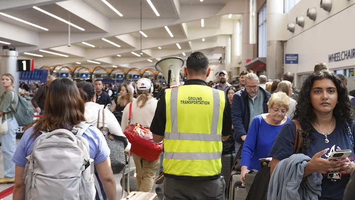 Un employé de l'aéroport aide les voyageurs à avancer dans les longues files d'attente à l'aéroport international Hartsfield-Jackson d'Atlanta, le 22 mars 2026, à Atlanta, en Géorgie. 
