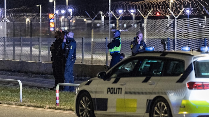 Sur le terrain d'un aéroport, la nuit, des policiers danois regardent vers le ciel.