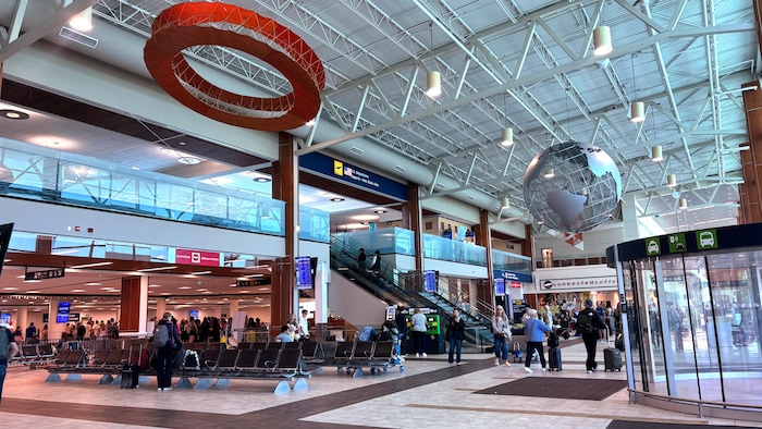 Une vue intérieure de l'aéroport, avec des banquettes et des objets d'art suspendus au plafond.