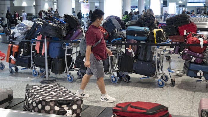 Un passager cherche ses bagages parmi une pile de valises et de sacs non réclamés à l'aéroport international Pierre-Elliott-Trudeau, à Montréal.