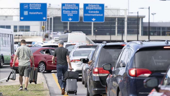 Deux passagers traînent leur valise au milieu des embouteillages à l'entrée de l'aéroport de Montréal.