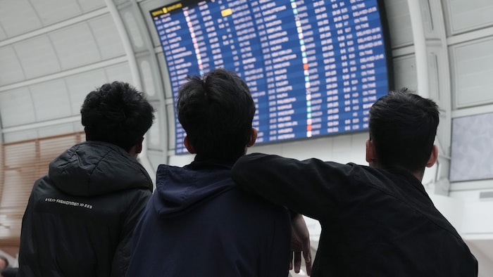 Des passagers regardent le tableau des départs à l'aéroport.