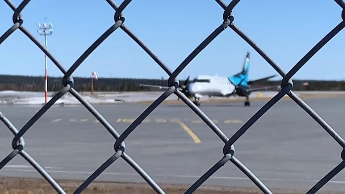 Un avion immobile sur une piste d'atterrissage derrière une clôture.