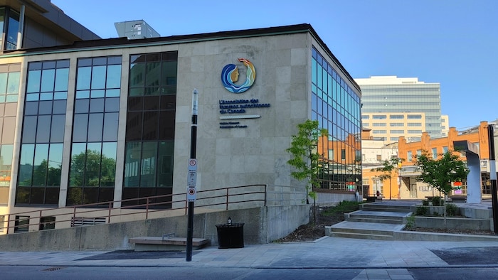Un bâtiment vitré et de pierres grises avec le logo de l'association.
