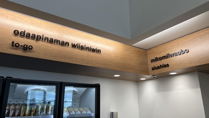 Des affichages en haut de différentes sections du dépanneur, écrits en anishinaabemowin et en anglais
