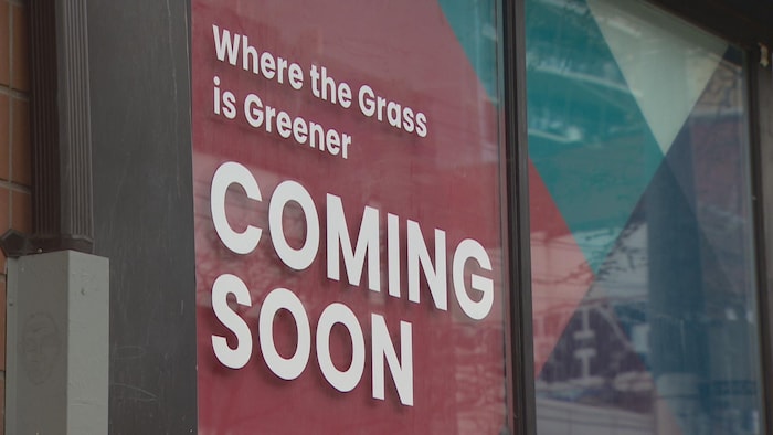 Une grande affiche rouge, collée dans une vitrine, qui indique qu'un magasin de cannabis sera bientôt ouvert à cet endroit.
