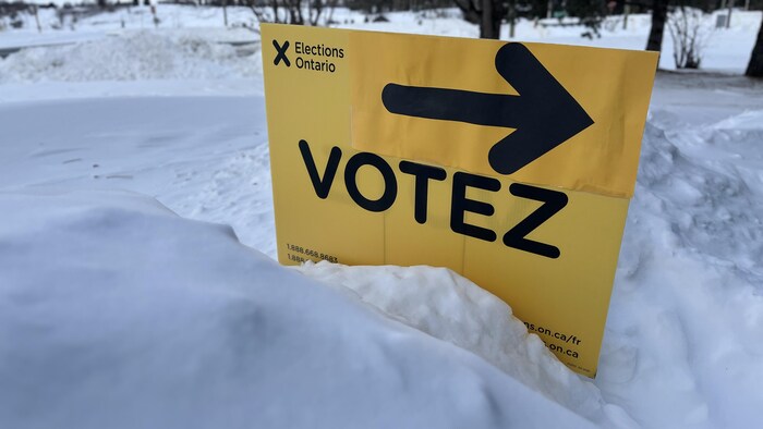 Une affiche jaune d'Élections Ontario sur laquelle il est écrit « Votez » est plantée dans la neige devant un édifice à bureaux, à Plantagenet, dans l'est ontarien.