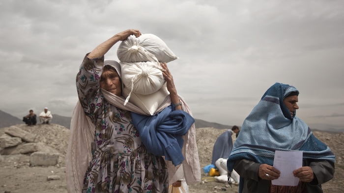 Une femme afghane transporte des sacs de nourriture.