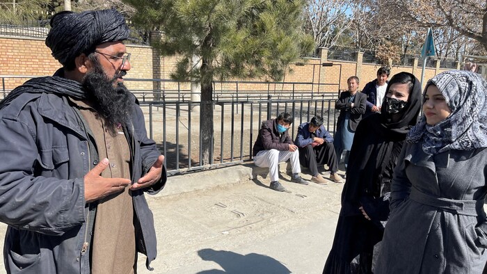 Un membre du régime taliban s'entretient avec des étudiantes devant l'Université de l'éducation de Kaboul.