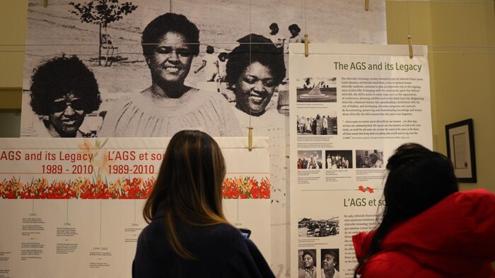Deux femmes de dos consultent un panneau dans un musée qui explique le travail d'une société de généalogie.