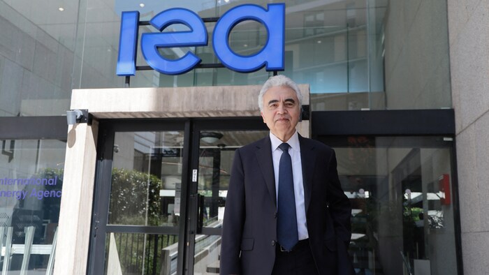 Un homme en costume et cravate se tient devant l'entrée du siège de l'Agence internationale de l'énergie.