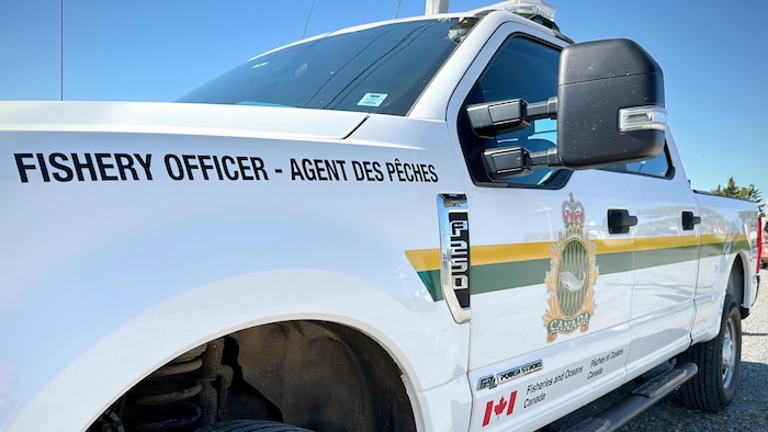 Une camionnette blanche stationnée décorée du logo de Pêches et Océans Canada et des mots « Agent des pêches ».
