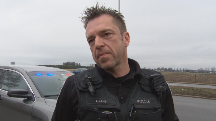 L'agent Phil Kane devant sa voiture de police à l'intersection du chemin Baseline et de l'avenue Fisher.