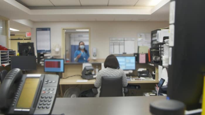 Une infirmière parle avec une agente administrative assise, de dos, à son bureau dans un hôpital.