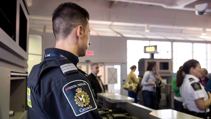 Un agent frontalier du Canada observe les passagers à une porte d'embarquement dans un aéroport