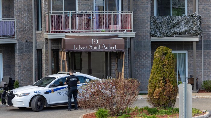 Un policier près d'un véhicule du Service de police de la Ville de Québec est près de l'entrée d'un immeuble.