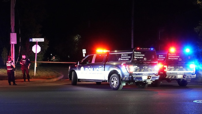 Des véhicules de police et des policiers devant un périmètre de sécurité.