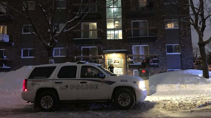 Un véhicule utilitaire sport du Service de police de la Ville de Québec est stationné devant un immeuble d’appartements. La photographie a été prise de soir, en hiver.