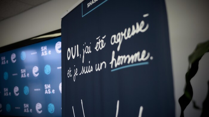 Une affiche indique le slogan de la campagne : «Oui, j'ai été agressé et je suis un homme.»