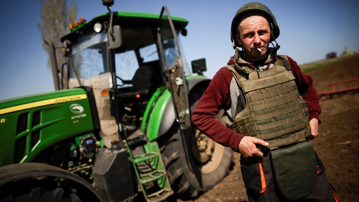 مزارع يرتدي سترة مضادة للرصاص يدخن سيجارة بالقرب من جرار في حقل.