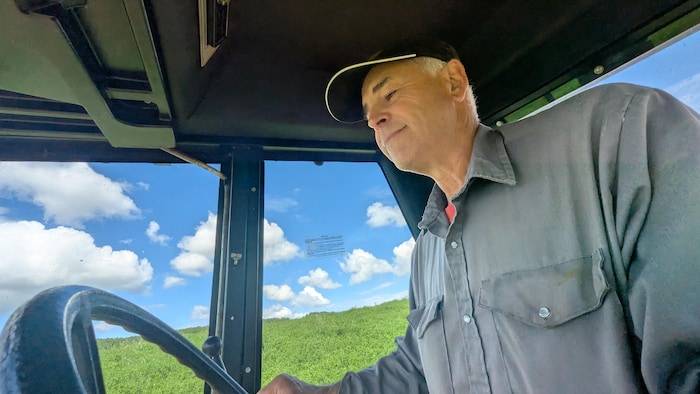 Ronald Cormier est assis dans sa machine agricole. Il conduit.