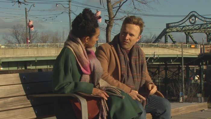 Deux personnes assises sur un banc de parc avec en arrière-plan la ville de Toronto. 