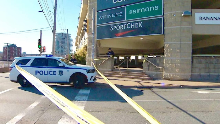 Un périmètre de sécurité autour du bâtiment faisant partie du centre commercial. Plusieurs policiers sont sur la scène, ainsi qu'un véhicule de police.