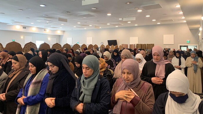 Des dizaines de femmes portant le hijab, la tête baissée, dans une mosquée, se recueillent à la mémoire d'un jeune homme décédé. 