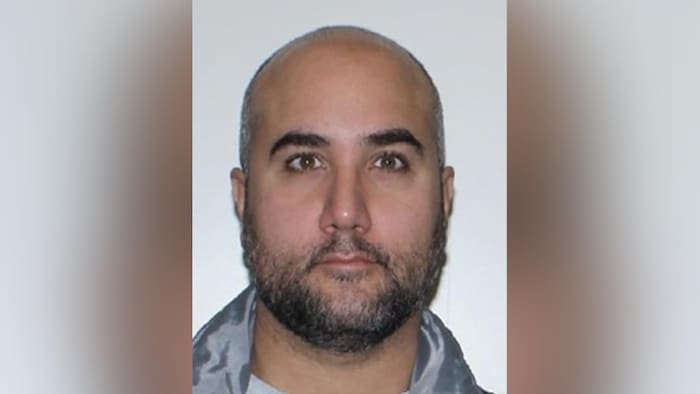 L'homme a le crâne dégarni et porte une courte barbe.