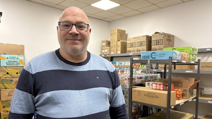 Un homme pose en souriant devant des étagères où sont empilées des denrées.