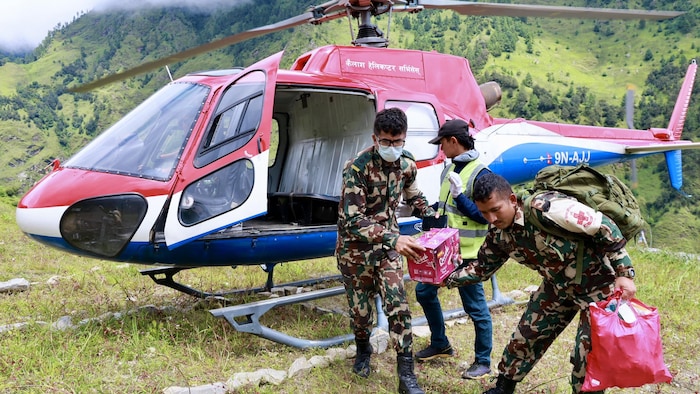 Des militaires sortent des sacs et des boîtes d'un hélicoptère.