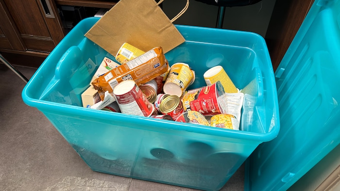 Un contenant rempli de boîtes de conserve et des cartons de soupe de style ramen. 