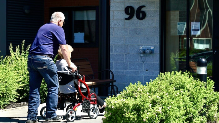 Une personne âgée est assise sur son déambulateur, alors qu'une autre personne la pousse.      