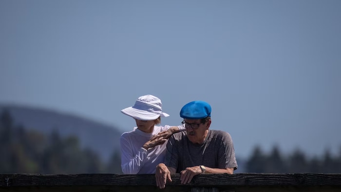 Un homme et une femme âgés penchés sur une balustrade en bois, par un temps chaud.