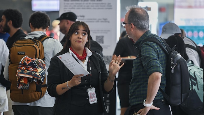 Une agente d'Air Canada, à gauche, discute avec un homme alors que les agents de bord d'Air Canada sont en grève à l'aéroport international Pierre-Elliott-Trudeau de Montréal, le samedi 16 août 2025.