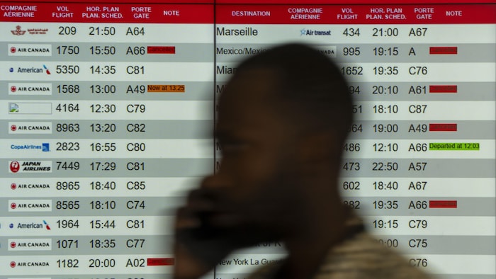 Un homme parlant au cellulaire passe devant un tableau sur lequel des vols annulés et retardés sont affichés.