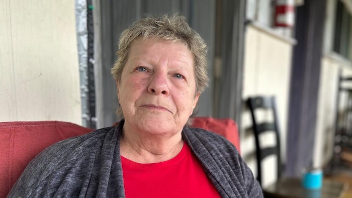 Une femme âgée aux courts cheveux blond cendré est assise dans une chaise rouge, sur la véranda d'un motel.