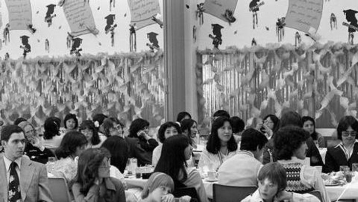 Une photo et noir et blanc de personnes assises à des tables dans une salle décorée.