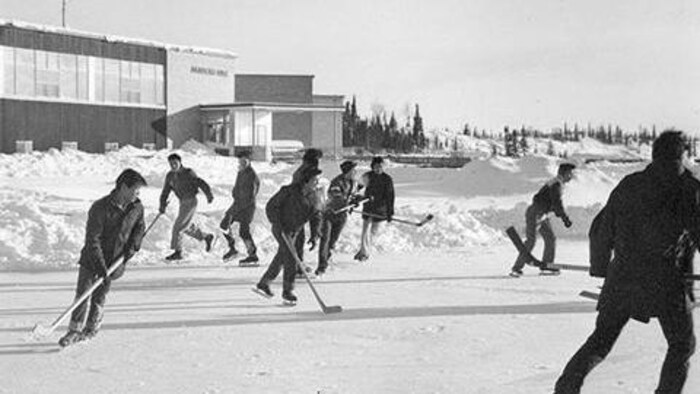 Une image en noir et blanc de personnes sur un patinoire devant Akaitcho Hall.