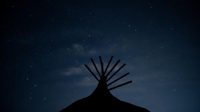 Un ciel étoilé et un bâtiment au premier plan.