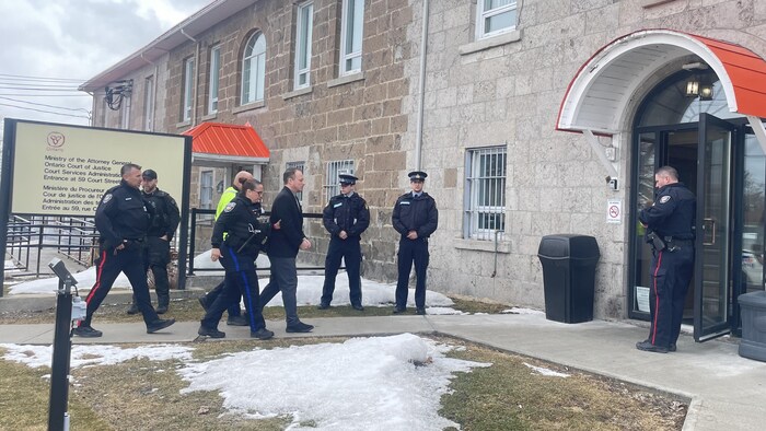 Alain Bellefeuille entre au palais de justice, escorté de policier. 